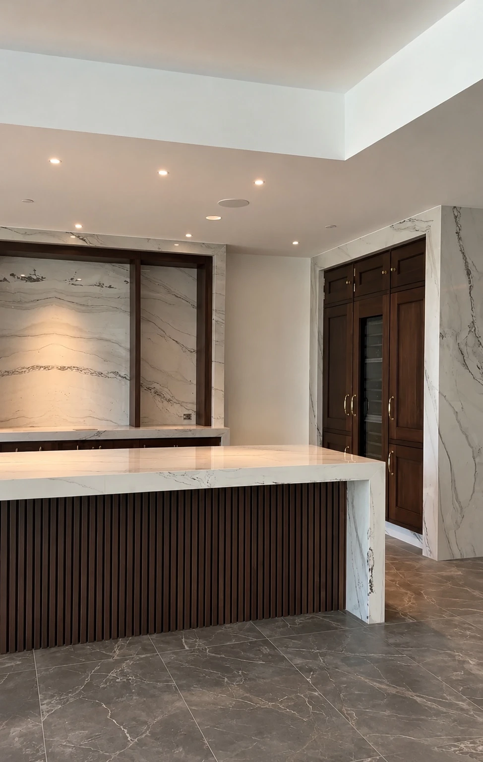 Luxury bar with white marble waterfall countertop, dark wood slat detailing and custom walnut cabinetry by Obsidian Walls